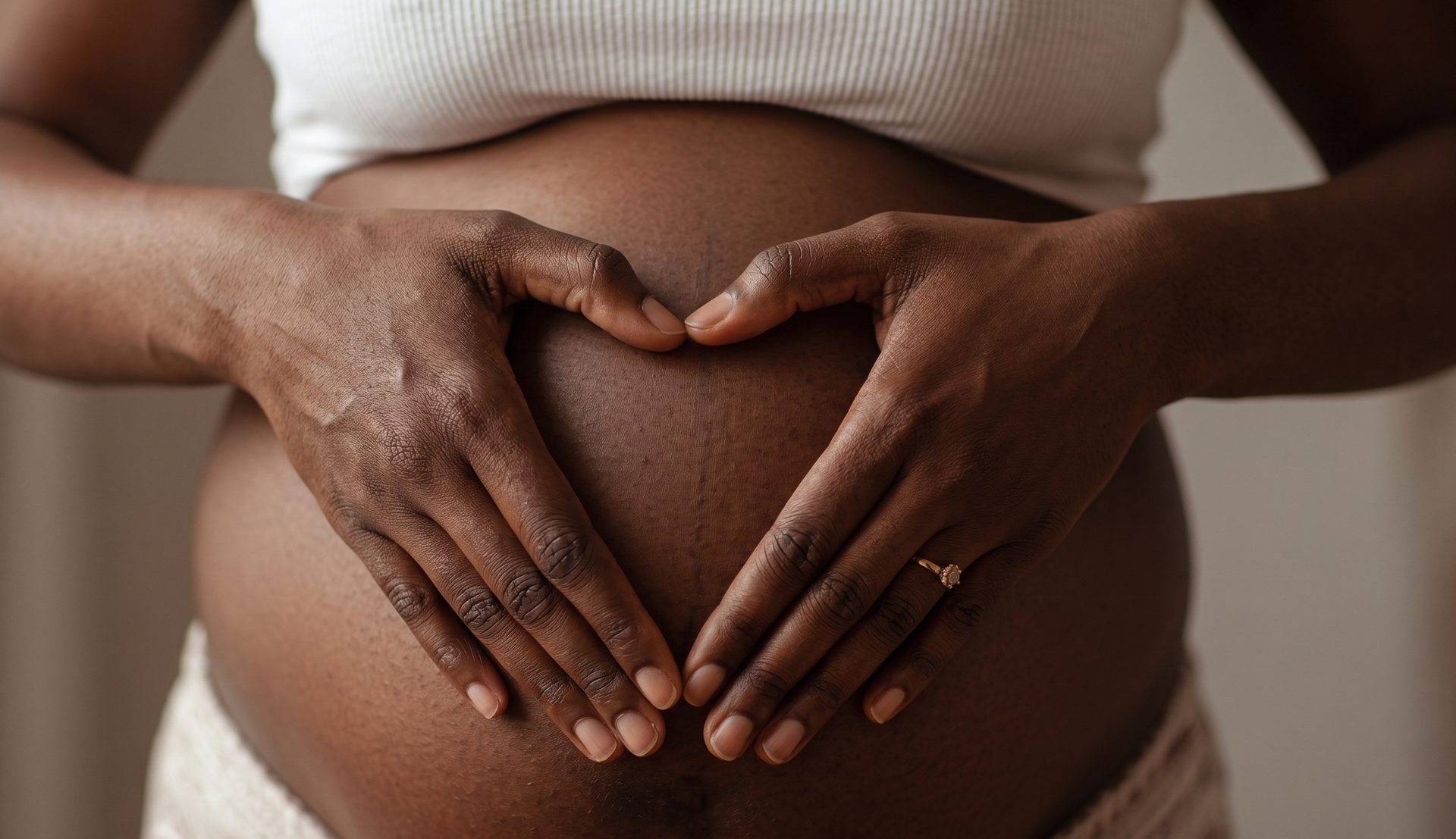A pregnant woman with her hands forming a heart shape on her belly.